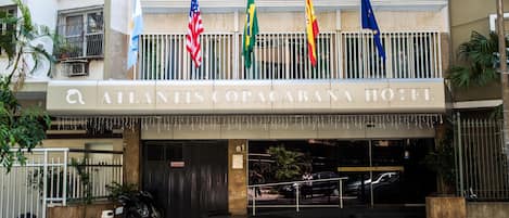 The exterior of Atlantis Copacabana Hotel with multiple flags, a gated entrance, and a staircase leading to the entrance.