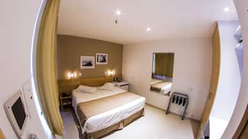 Een hotelkamer met een bed, nachtkastje, lamp, spiegel en een raam met gordijnen.