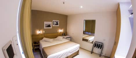 Una habitación de hotel con cama, mesita de noche, lámpara, espejo y ventana con cortinas.