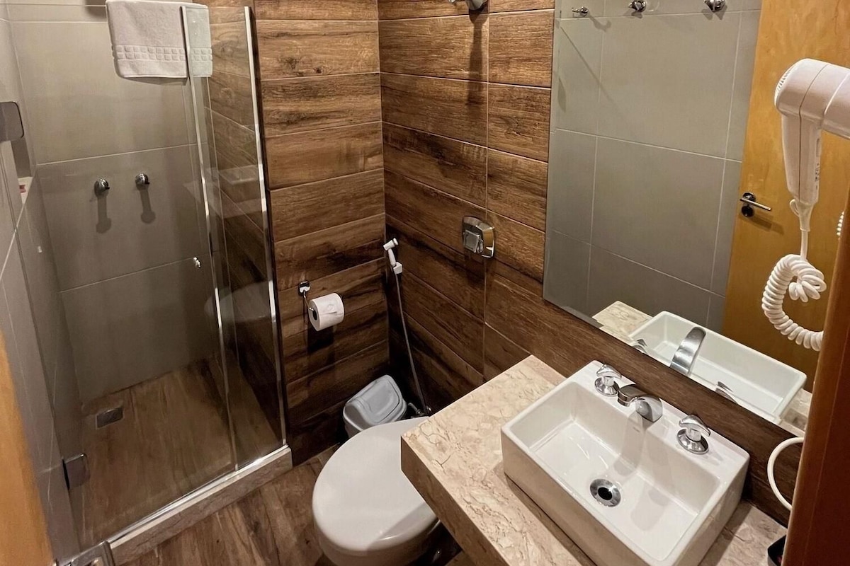 Un baño moderno con cabina de ducha de vidrio, inodoro, lavabo con espejo y secador de pelo.