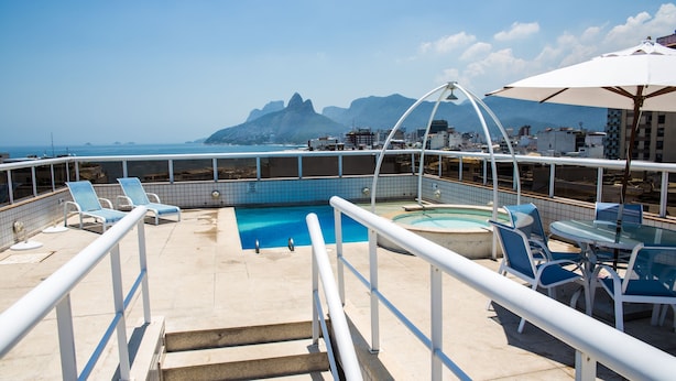 Zona de piscina en la azotea con vistas a montañas, sillas de descanso y una mesa con sombrillas.