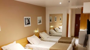 Habitación de hotel con cuatro camas individuales, cabecera de madera, televisor de pantalla plana y cuadros en la pared.