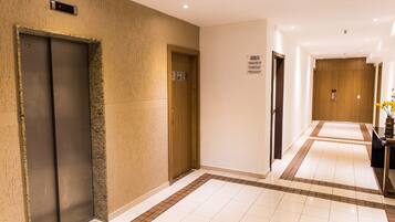 A hotel corridor with an elevator, a wooden door, and a sign with symbols.