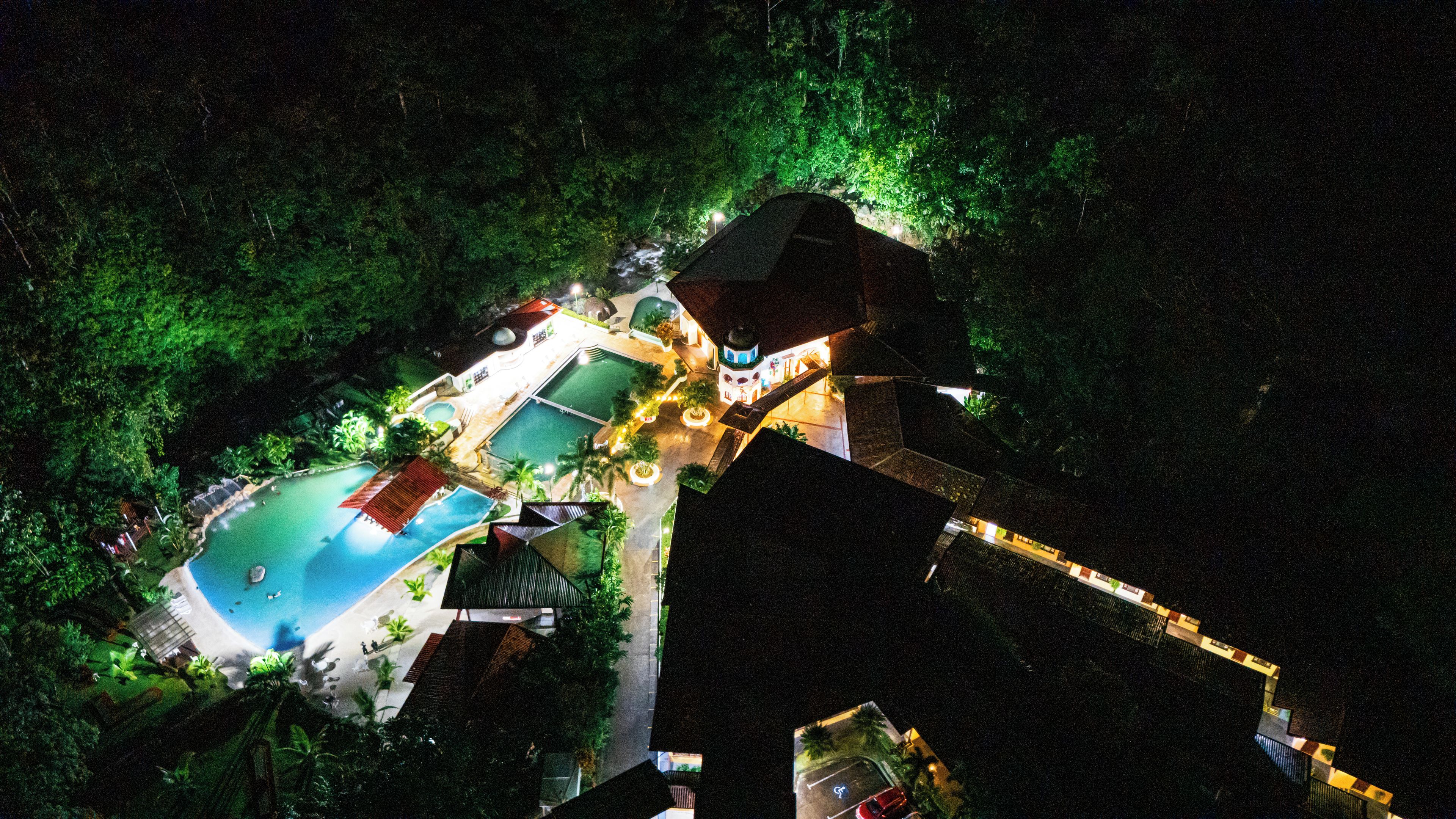 An aerial view of a resort with multiple swimming pools, a large building with a dome, and surrounding lush greenery.