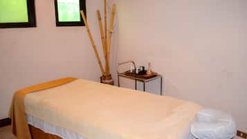 A room with a bed, a small table with a bottle and a container, and a wall-mounted mirror.