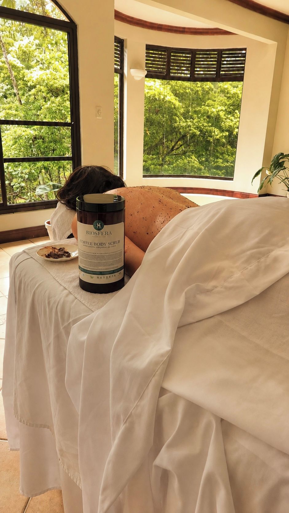 A room with a bed, a bottle of coffee body scrub, and a plate with food.