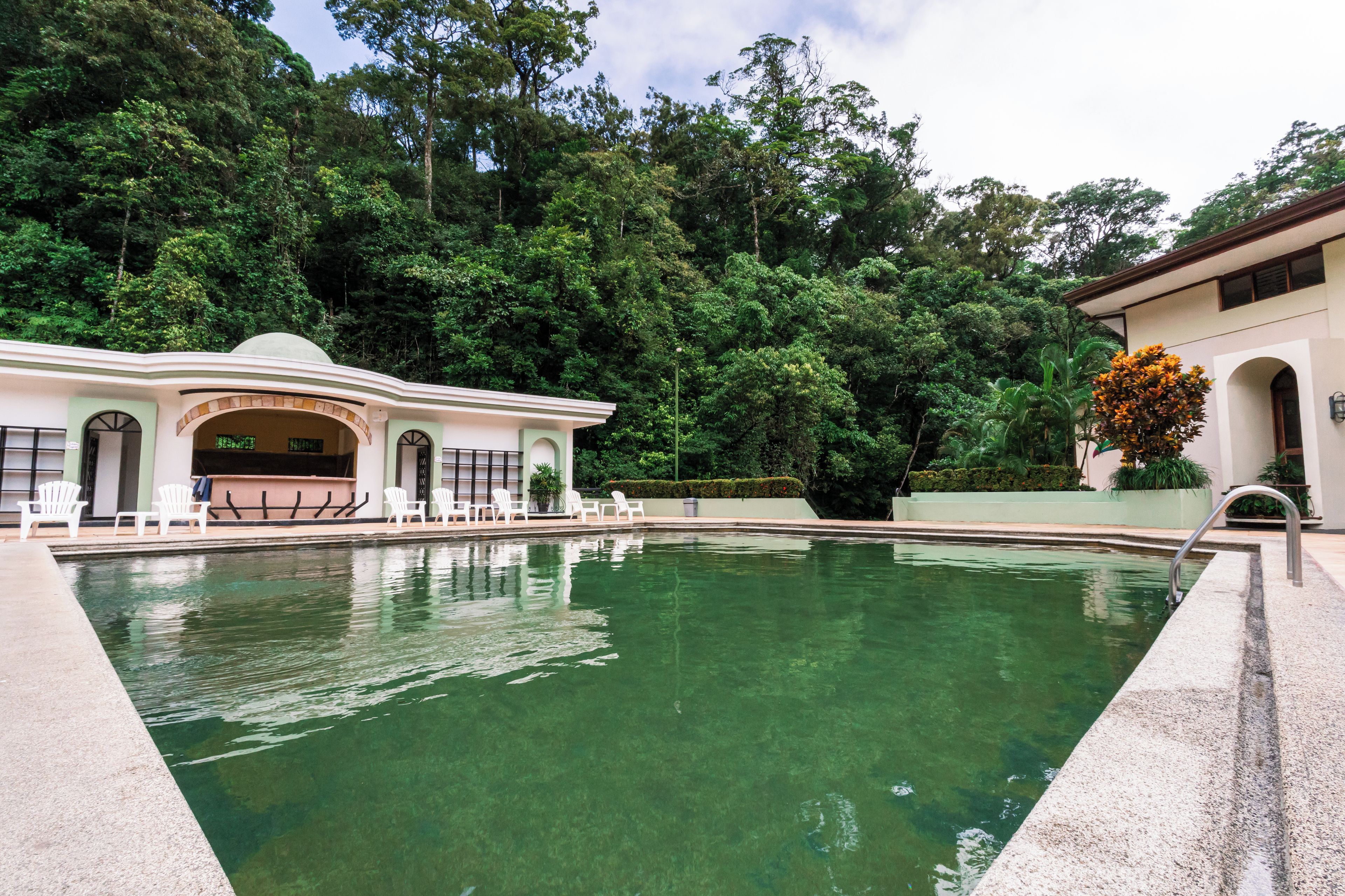 A swimming pool with clear water, surrounded by a building with a dome-shaped entrance and white chairs.