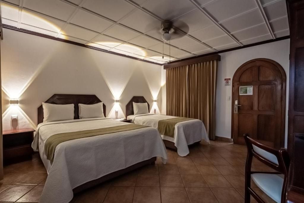 A hotel room with two beds, a wooden door, and a chair.