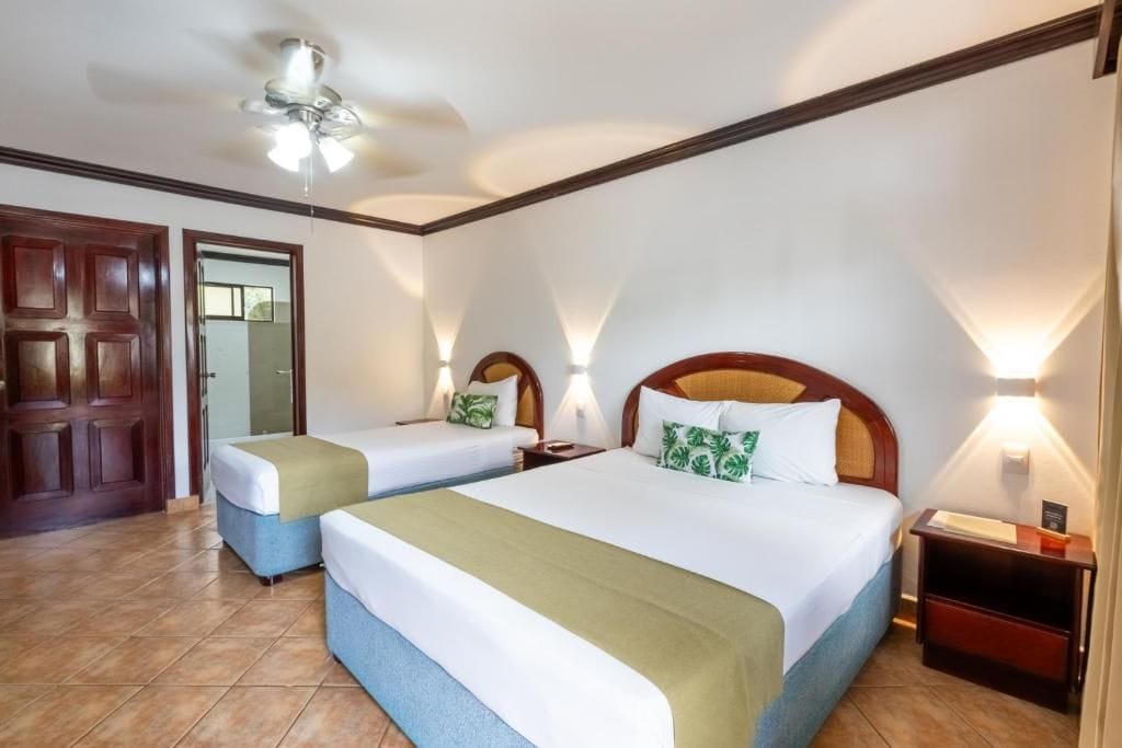 Une chambre d’hôtel avec deux lits, un ventilateur de plafond et une porte en bois.