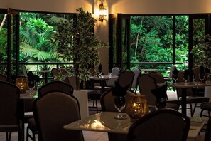 A restaurant with tables set for dining, surrounded by large windows with a view of dense greenery. - Hotel El Tucano Resort & Thermal Spa (La Palmeria)