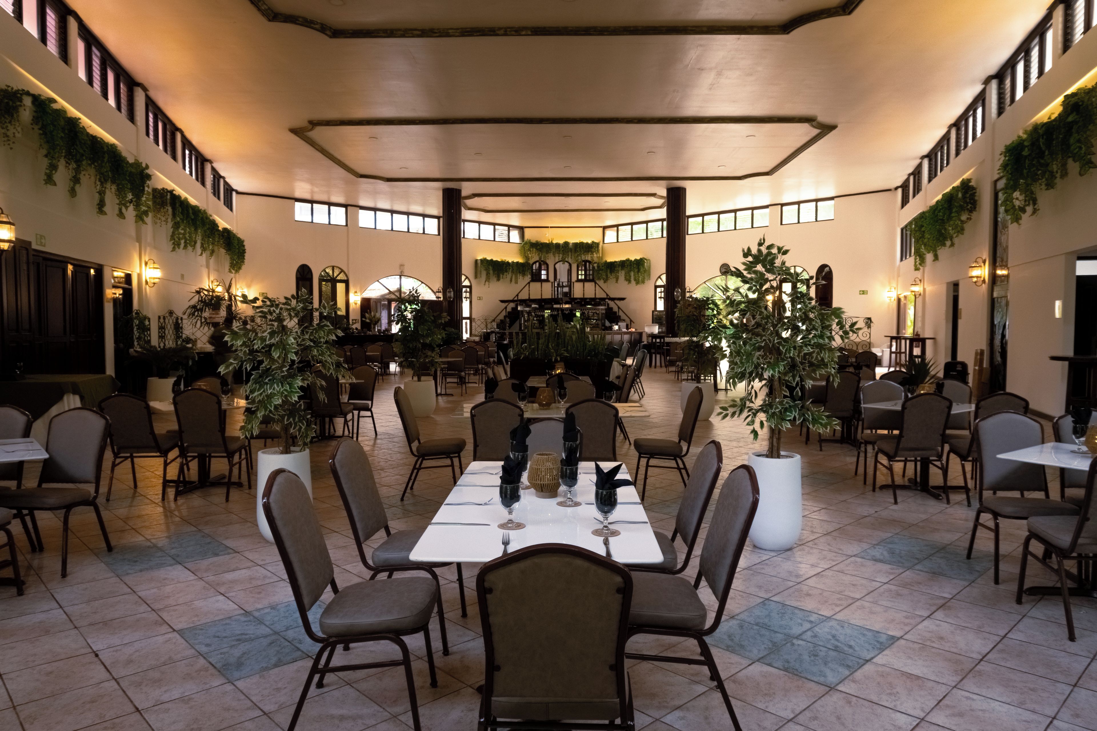 A spacious dining area with multiple tables and chairs, surrounded by walls adorned with greenery.