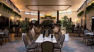 A spacious dining area with multiple tables and chairs, surrounded by walls adorned with greenery.