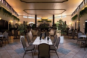 Un comedor amplio con varias mesas y sillas, rodeado de paredes decoradas con follaje.