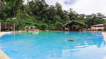 Piscina com águas cristalinas azuis, cercada por vegetação exuberante e um pequeno pavilhão.