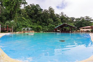Una piscina con agua azul cristalina, rodeada de exuberante vegetación y un pequeño pabellón.