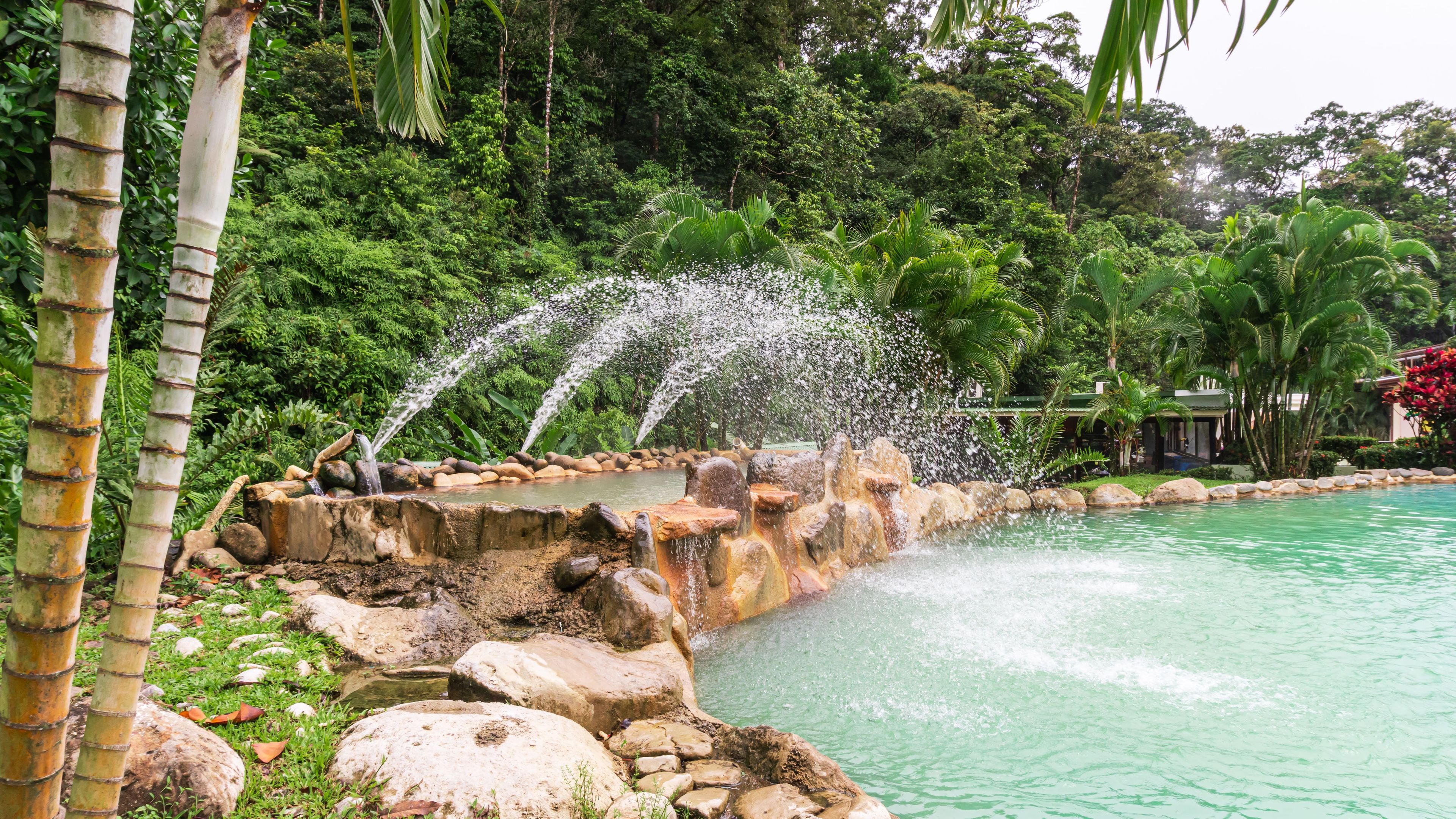A natural pool with a waterfall feature surrounded by rocks and lush greenery.