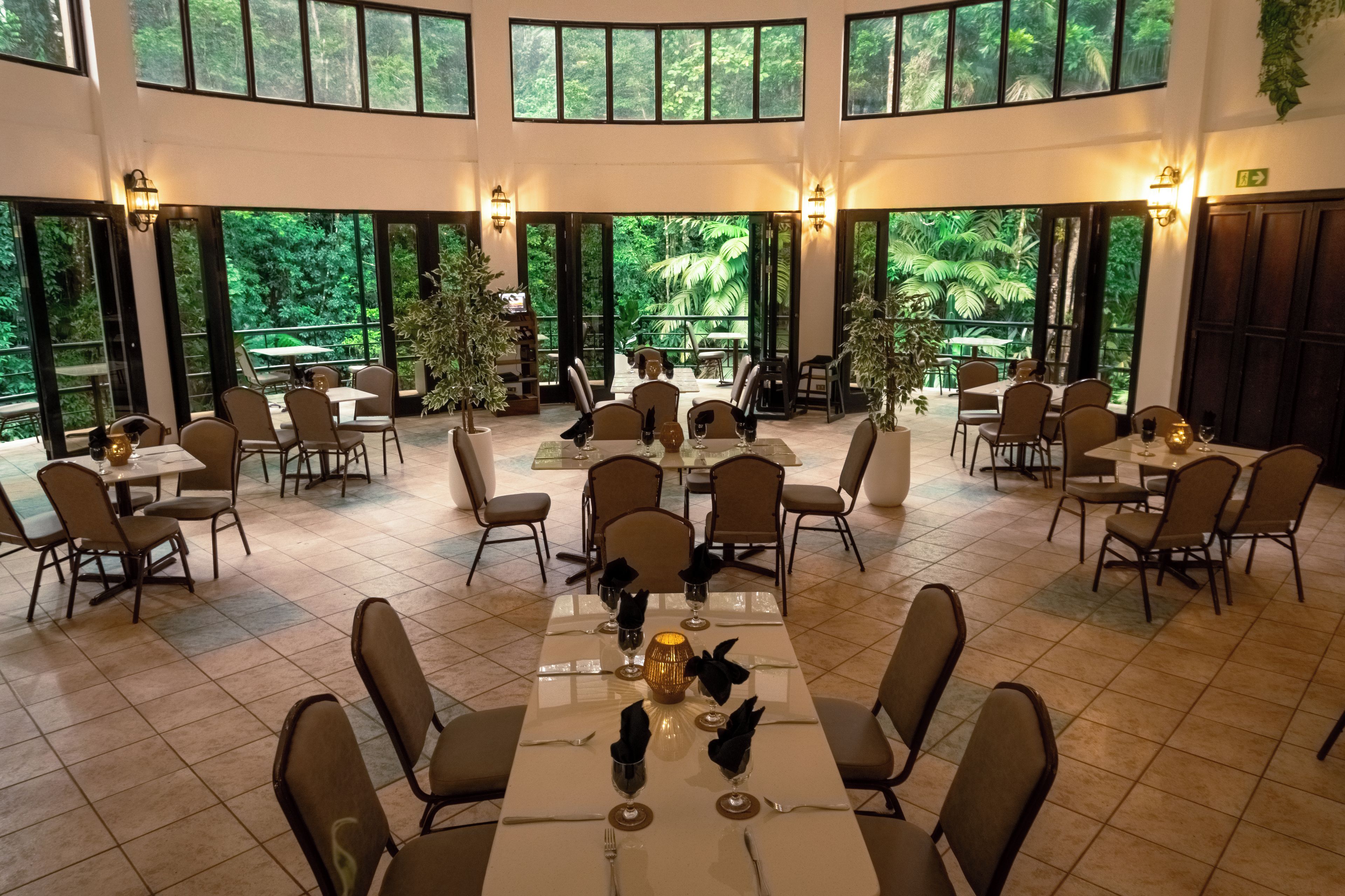 Un amplio comedor interior con varias mesas y sillas, ventanas grandes que ofrecen vistas a exuberante vegetación.
