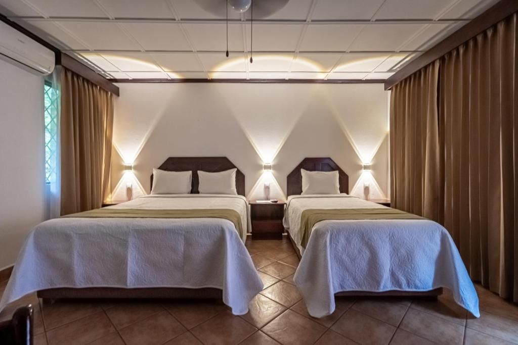 Habitación de hotel con dos camas, una mesita de noche y ventana con cortinas.
