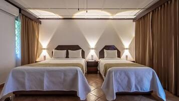 Habitación de hotel con dos camas, una mesita de noche y ventana con cortinas.