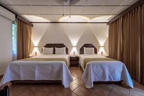 Ett hotellrum med två sängar, ett nattduksbord och ett fönster med gardiner.