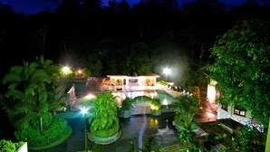 A resort with a swimming pool, lush greenery, and a well-lit building. - Hotel El Tucano Resort & Thermal Spa (La Palmeria)