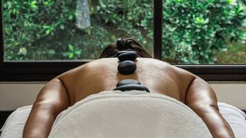 A person receiving a back massage with stones, with a window view of greenery.