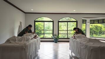 A room with two beds, large windows, and a potted plant.