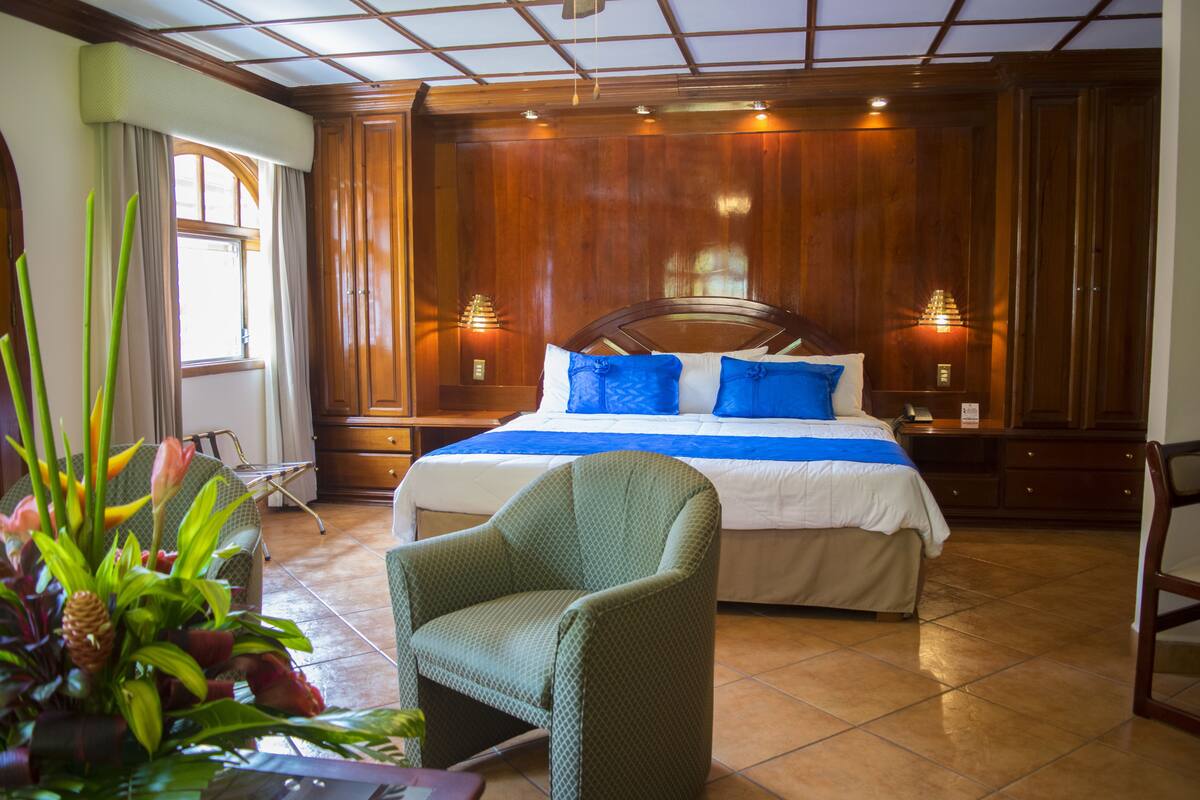 A hotel room with a large bed, wooden paneling, two bedside lamps, and a green armchair.