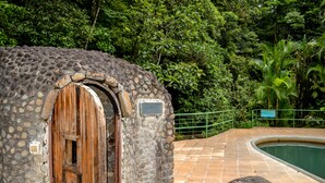 A stone building with a wooden door, a pool, and lush greenery in the background. - Hotel El Tucano Resort & Thermal Spa (La Palmeria)