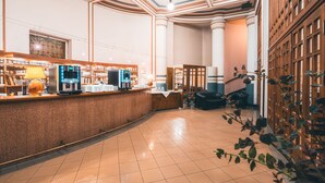 A hotel lobby with a reception desk, a coffee machine, and a seating area with a staircase. - Hotel Ariston & Ariston Patio (Prague)