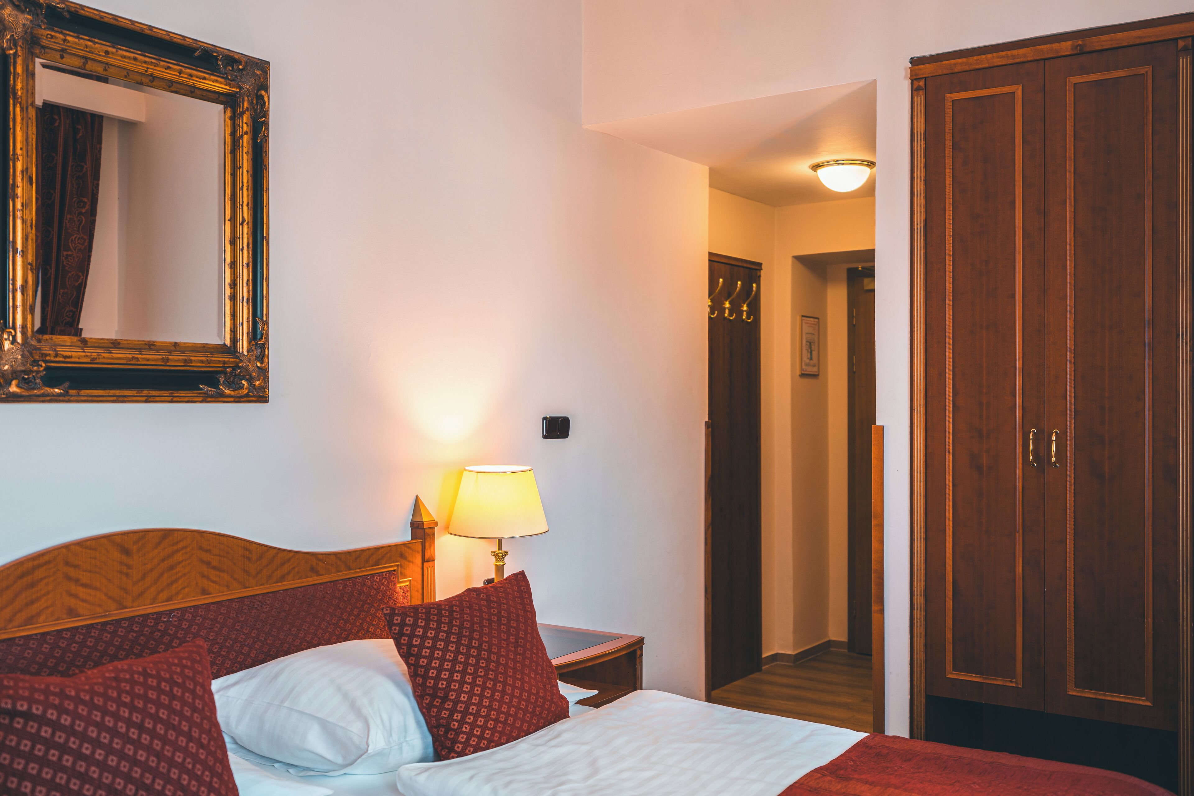 Una habitación de hotel con cama, mesita de noche con lámpara, espejo y armario.
