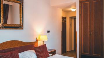 Una habitación de hotel con cama, mesita de noche con lámpara, espejo y armario.