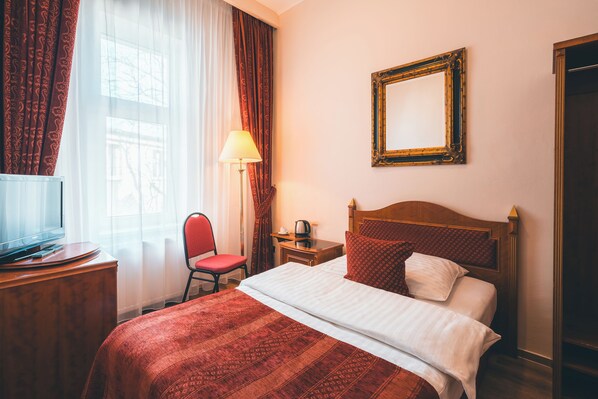 Habitación de hotel con cama, escritorio con televisor, silla, mesita de noche con lámpara y espejo en la pared.