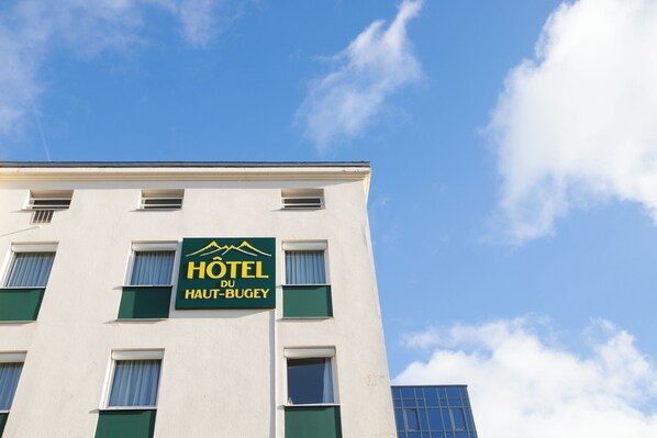 A hotel sign with the name "HOTEL DU HAUT-BUGEY" against a clear blue sky.