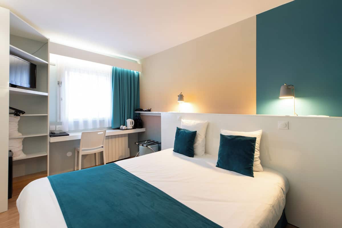 A hotel room with a bed, a desk, a chair, and a wardrobe.