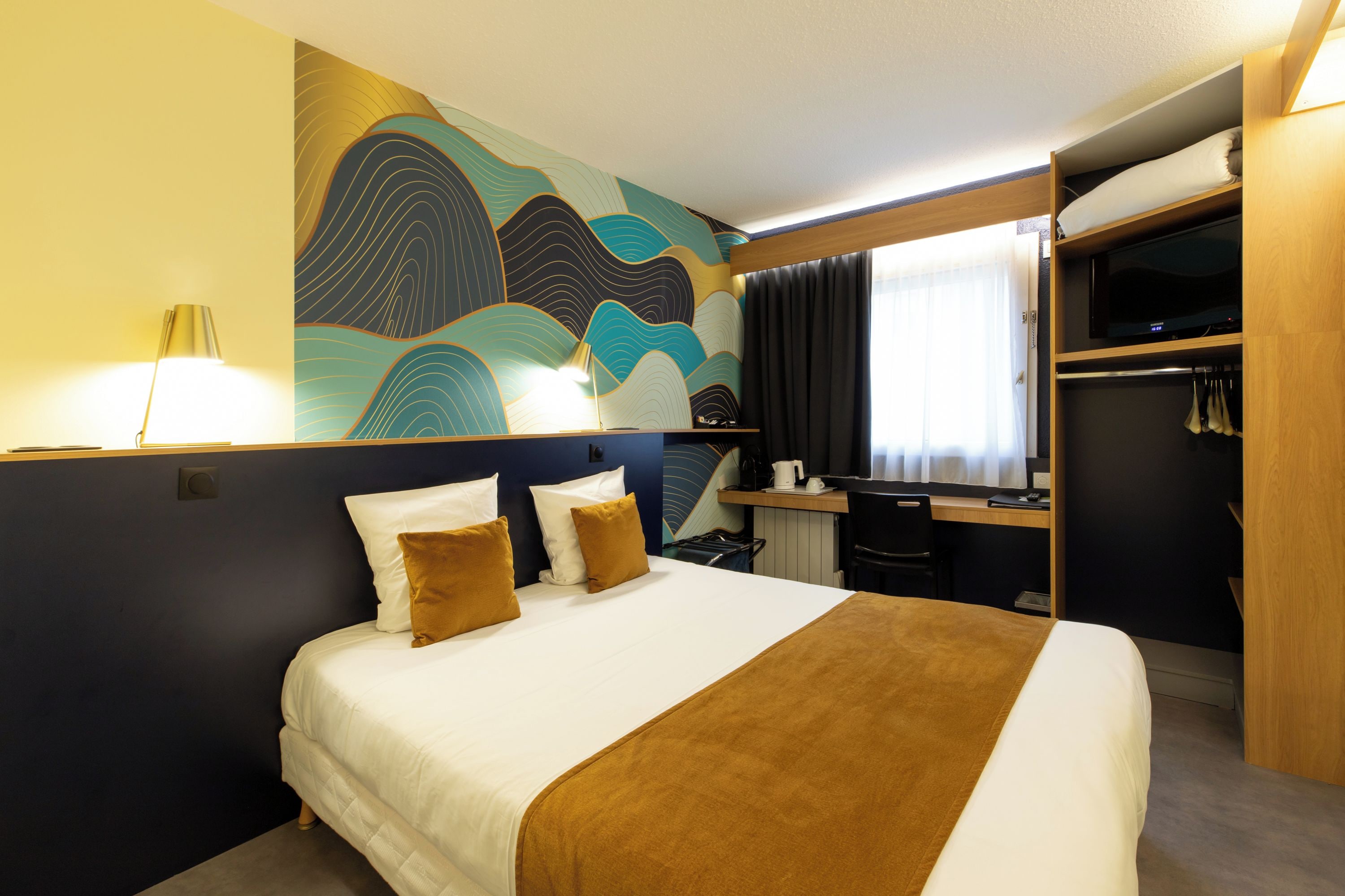 Habitación de hotel con cama, escritorio, armario y un gran mural abstracto en la pared.