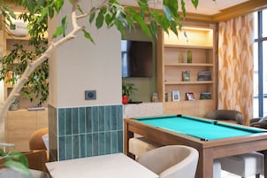 Una mesa de billar en una habitación con un mueble de madera, un televisor y una planta.