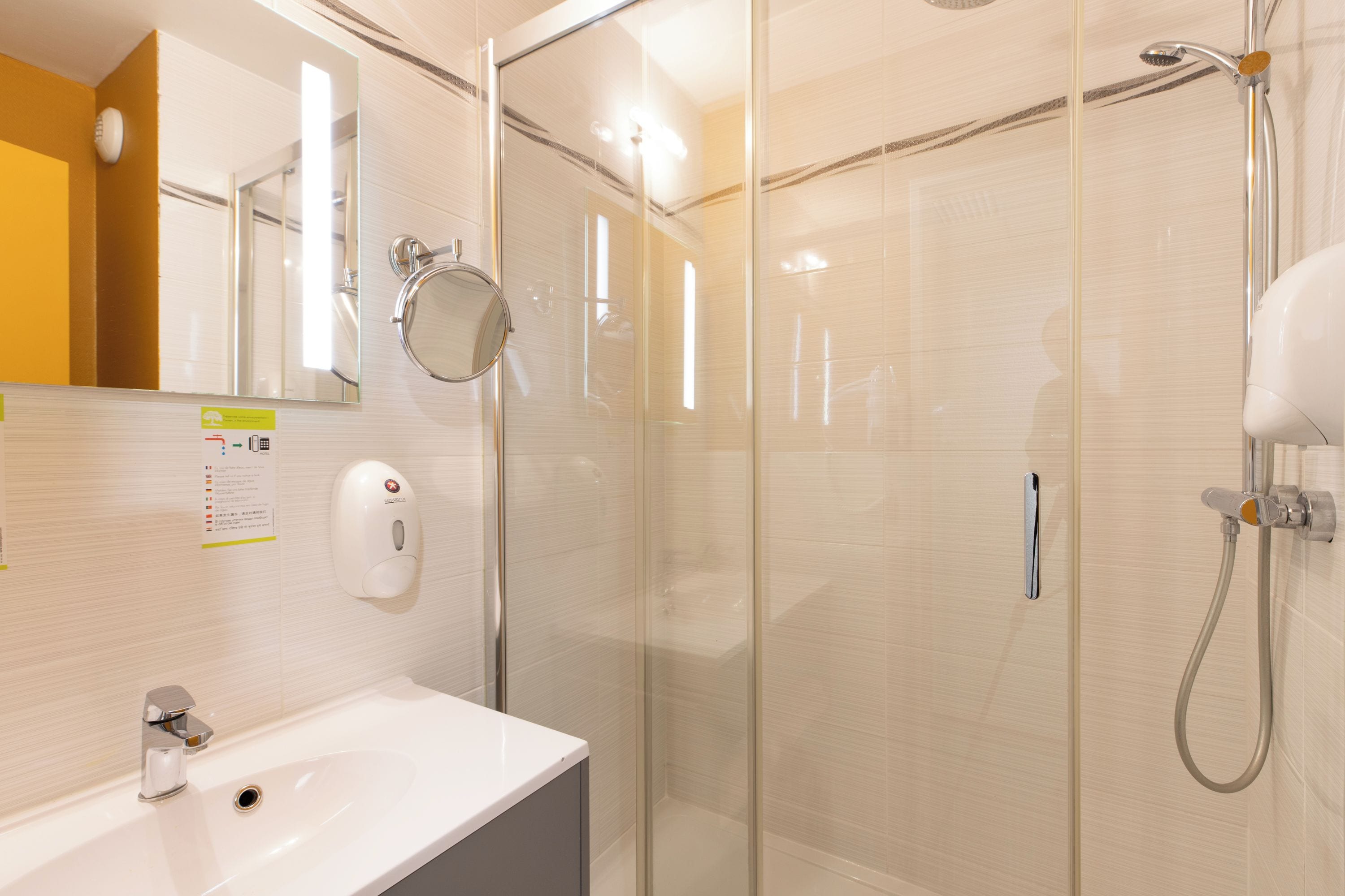 Une salle de bain moderne avec une douche à parois de verre, un lavabo blanc et un distributeur de savon liquide.