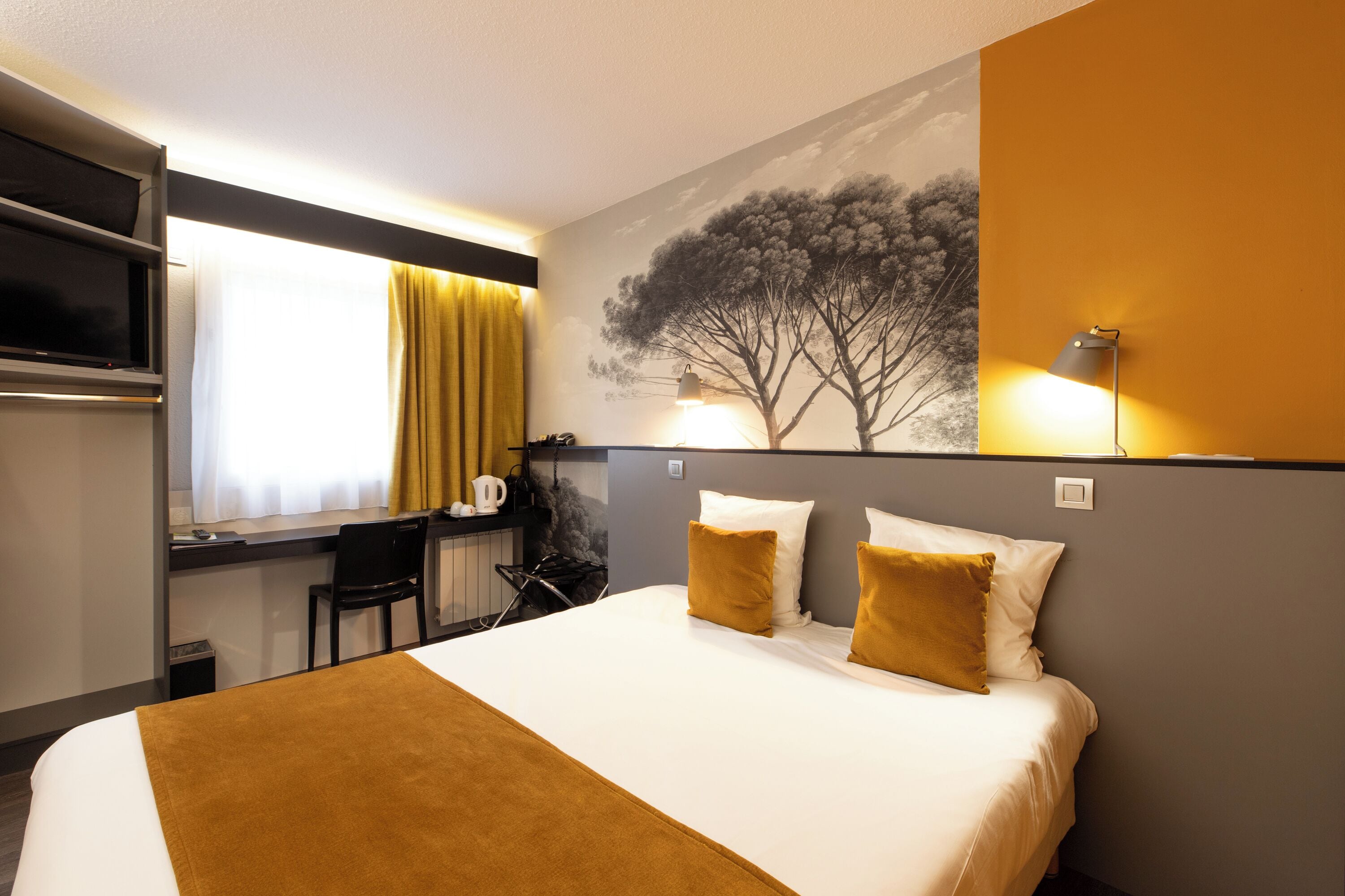 Une chambre d’hôtel équipée d’un lit, d  ’un bureau, d’une chaise, d’une télévision et d’une lampe fixée au mur.