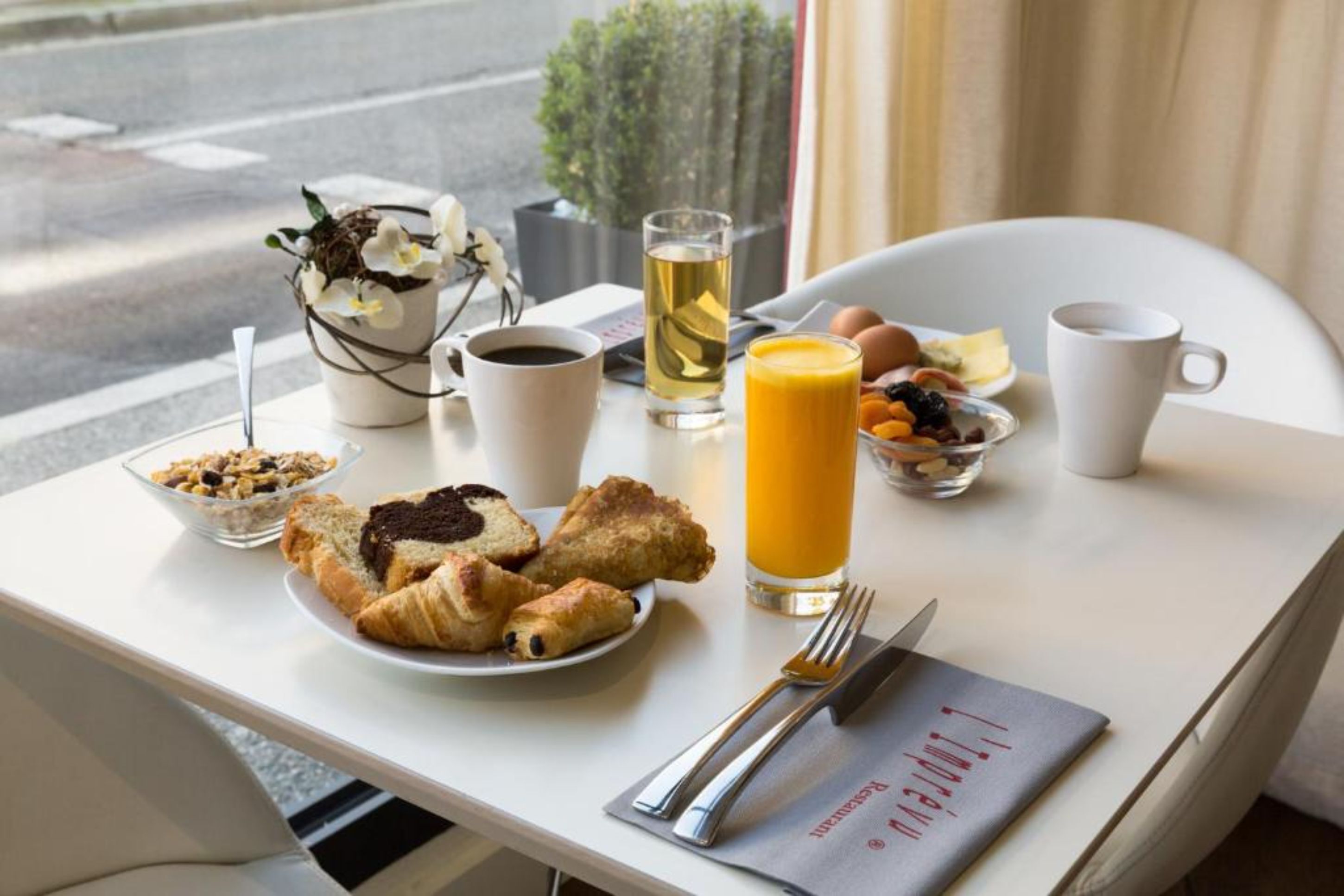 A breakfast table with croissants, a glass of orange juice, a cup of coffee, and a bowl of fruit.