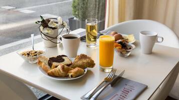 A breakfast table with croissants, a glass of orange juice, a cup of coffee, and a bowl of fruit.