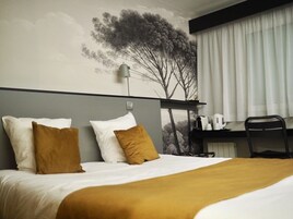 Una habitación de hotel con una cama, dos almohadas, un escritorio con silla y un mural en la pared.