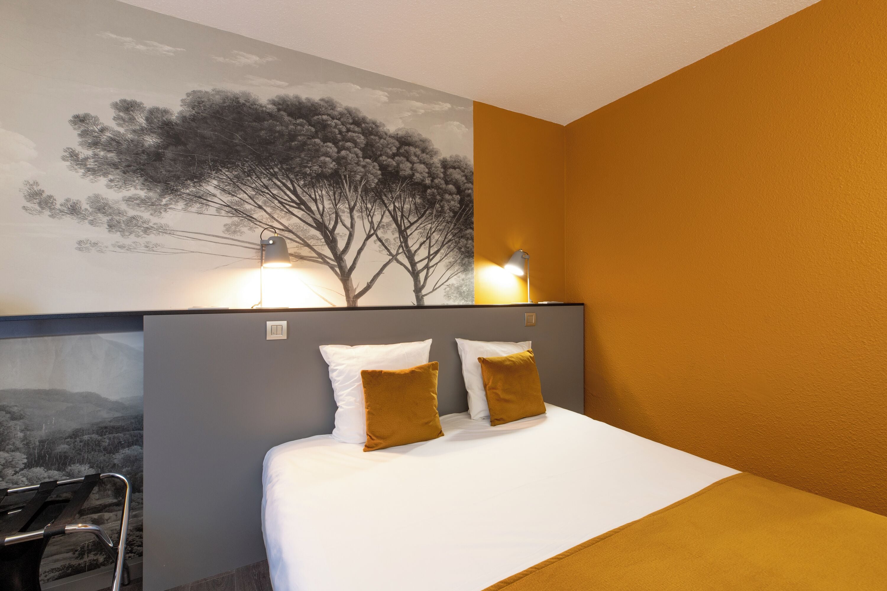 A hotel room with a bed, two pillows, a nightstand, a lamp, and a wall mural.