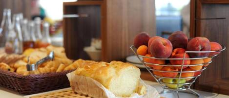 A breakfast buffet with bread, pastries, and a fruit bowl.
