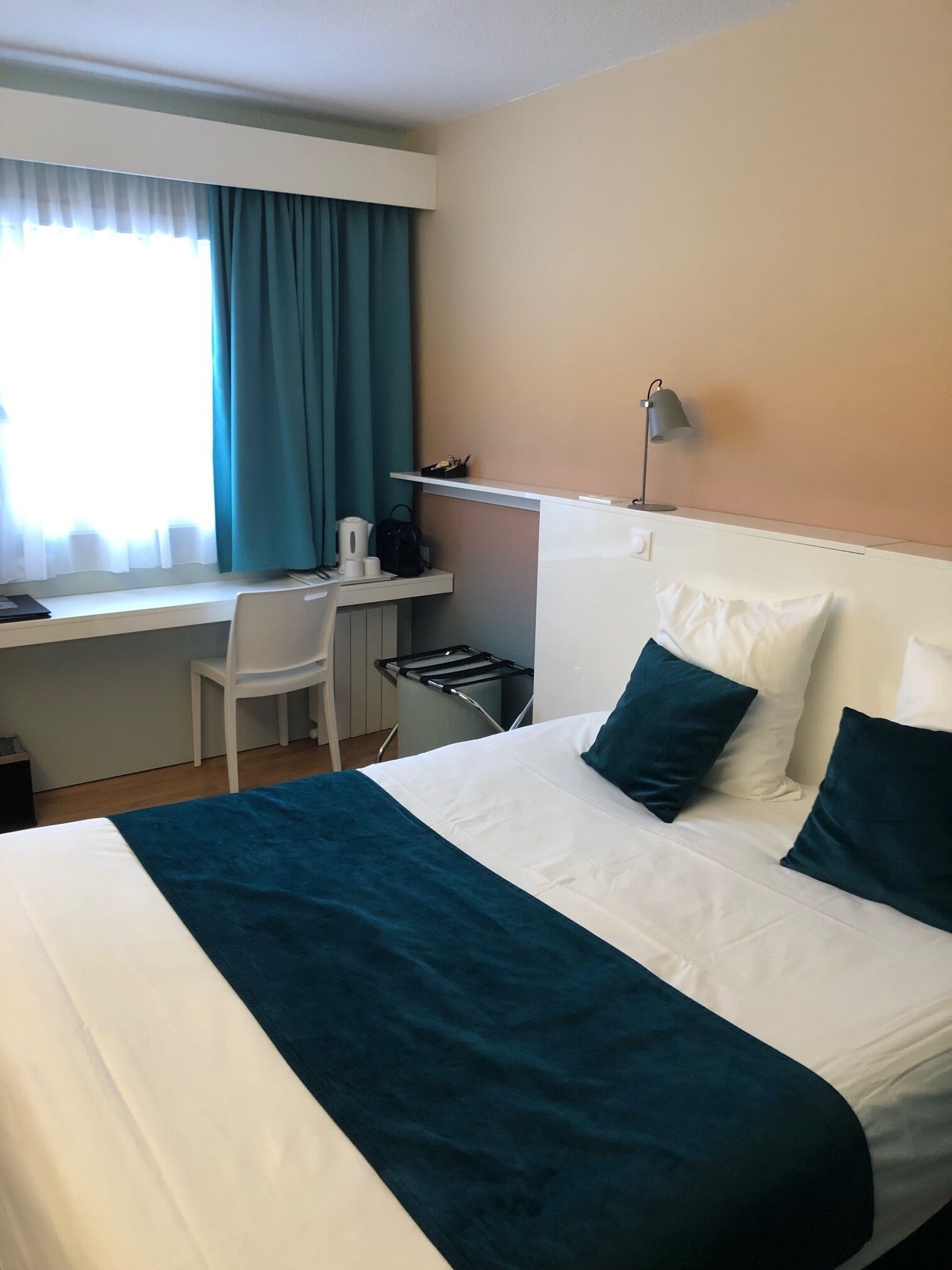 A hotel room with a bed, a desk, a chair, and a window with curtains.