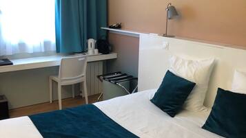 A hotel room with a bed, a desk, a chair, and a window with curtains.