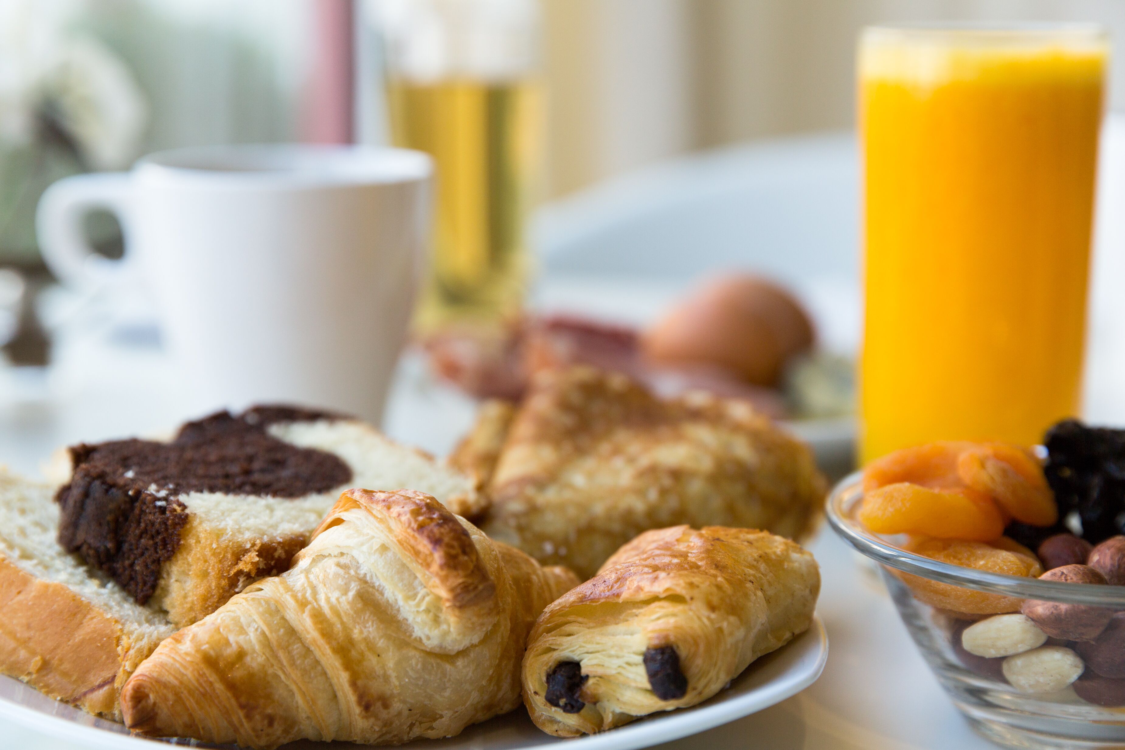 A breakfast plate with croissants, a muffin, and a bowl of nuts.