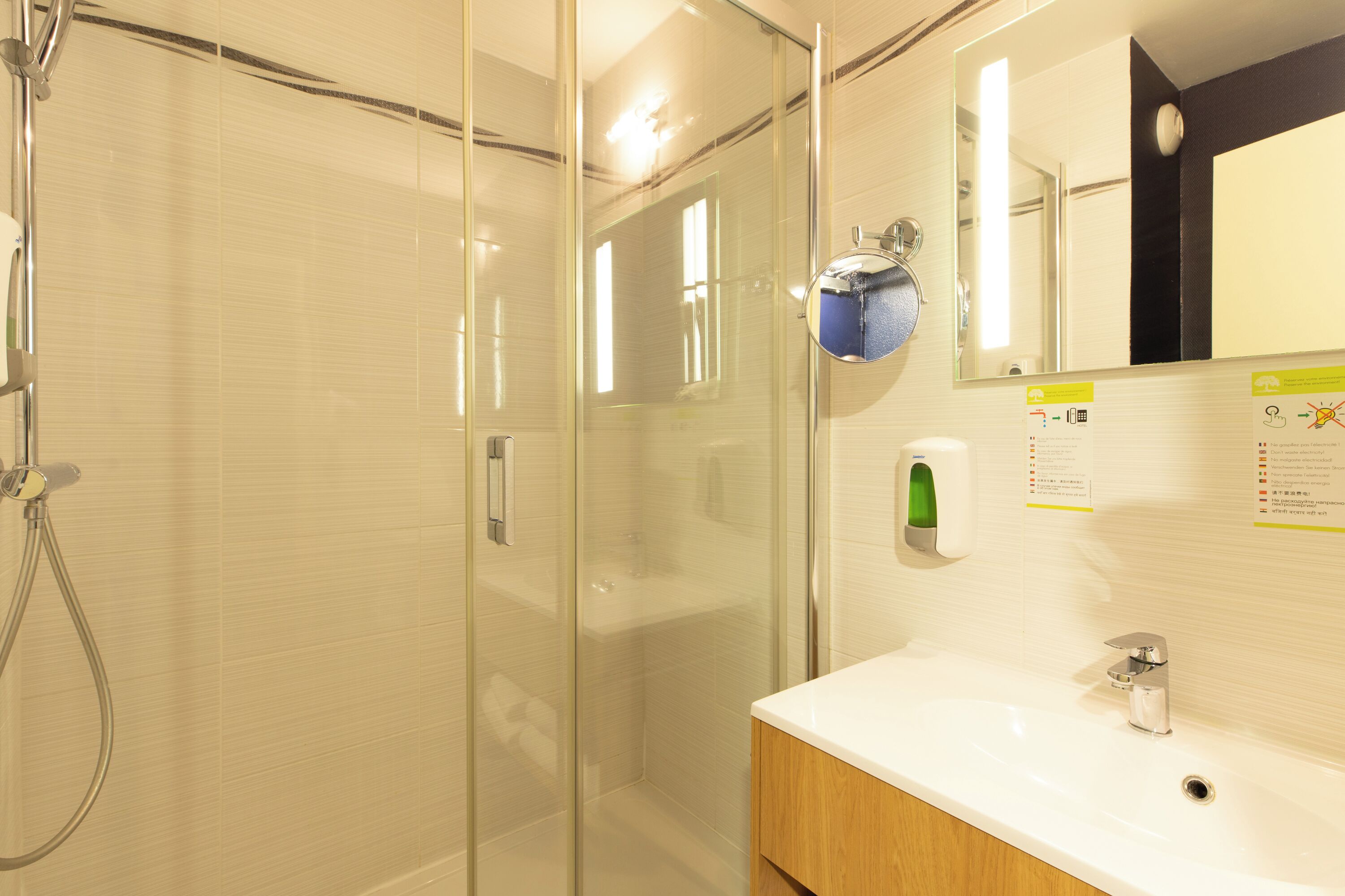 A modern bathroom with a glass-enclosed shower, a white sink, and a mirror with a clock.
