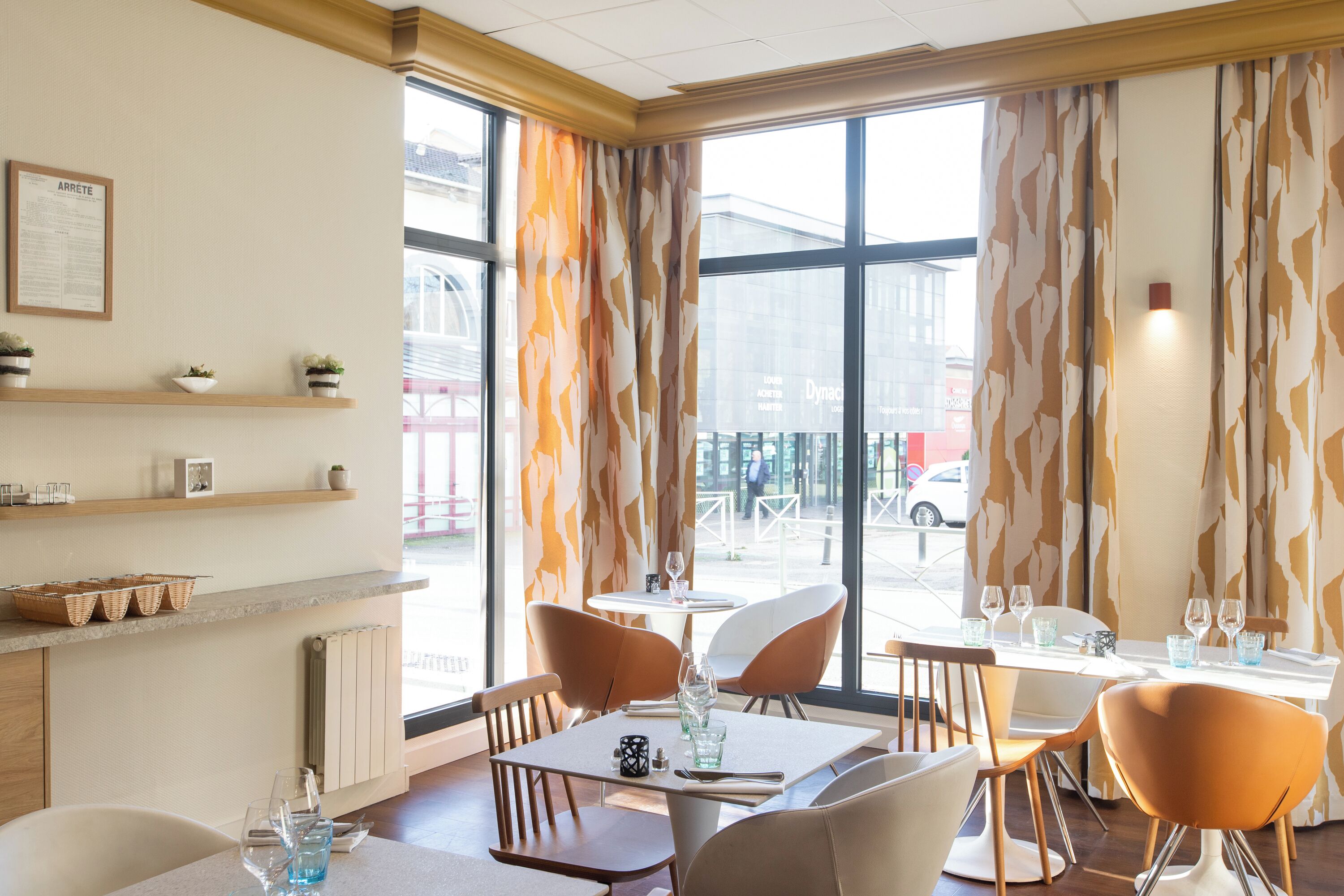 A restaurant with large windows, wooden chairs, and a table set with glasses and a vase.