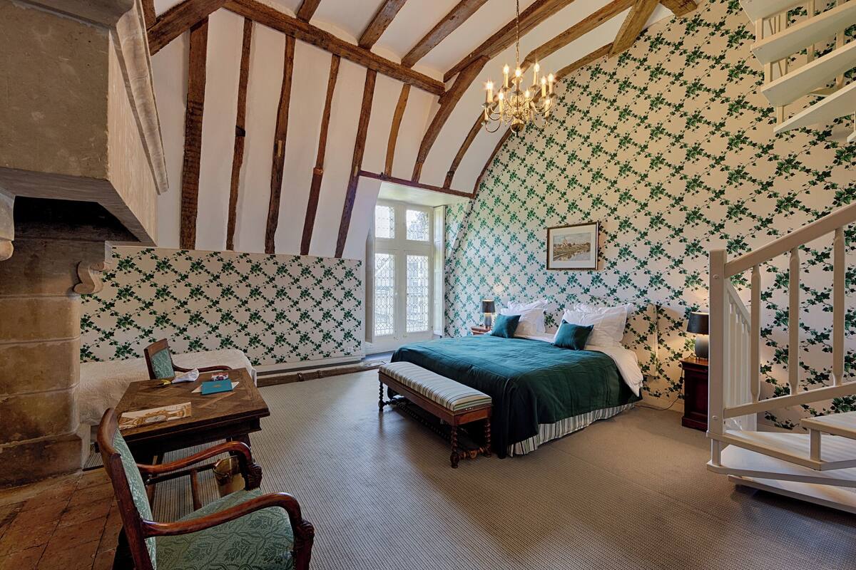 A bedroom with a large bed, a wooden bench, a table, and a chandelier.